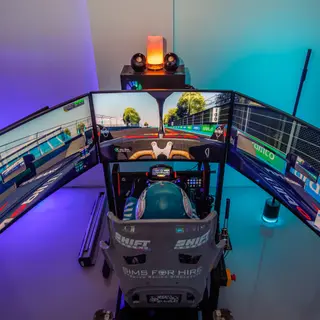 SimsForHire full-motion simulator with triple screens running the Miami circuit, helmeted driver at the wheel