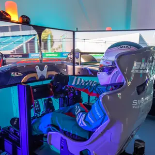Race-suited driver in a SimsForHire full-motion rig with the Miami circuit on triple screens