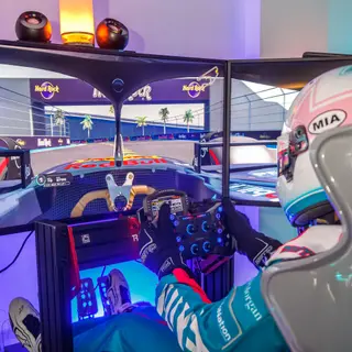 Over-the-shoulder view of a helmeted driver at the wheel with Hard Rock branding on screen